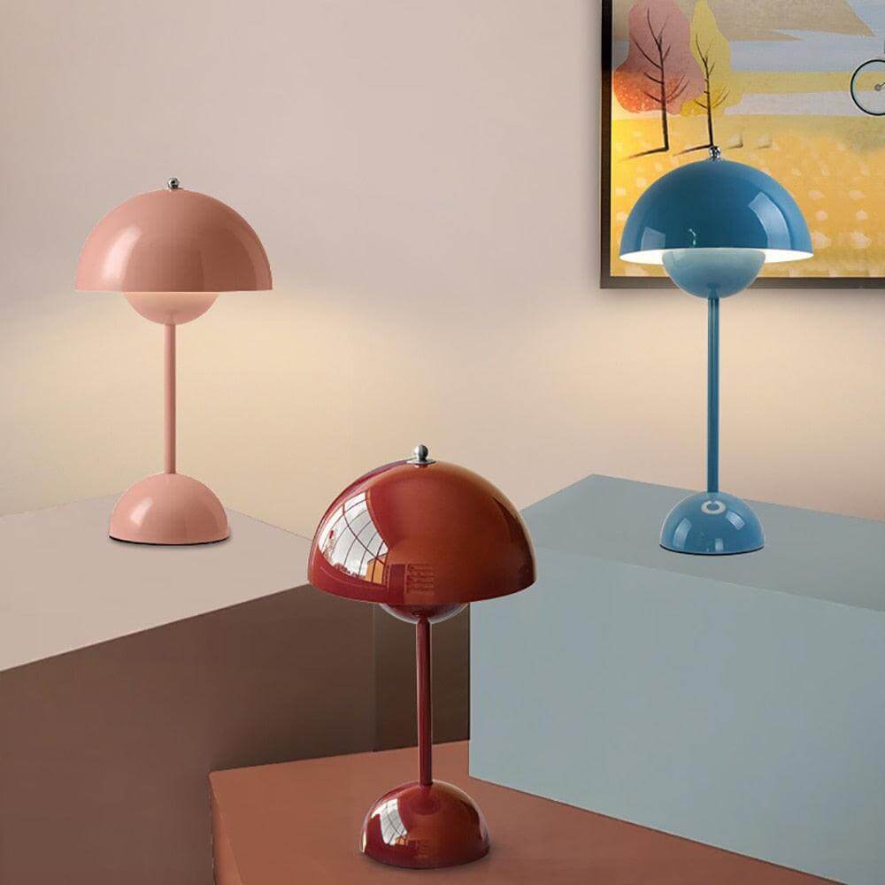 Pink, dark red and dark blue flowerpot vp9 portable rechargeable lamp sitting on tables with picture in background.